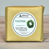 yuletide goat milk soap bar by brigid trading company bar of soap wrapped in brown kraft paper on a neutral surface with yuletide goat milk soap label depicting a christmas wreath