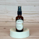 the florist room and linen spray Brown spray bottle labeled 'The Florist' on a white pedestal with a wooden background