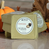 Samhain goat mil soap bar by brigid trading company in front of pumpkins and autumn leaves on a light colored reflective surface