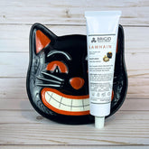 Black cat-shaped plate with a tube of Brigid Samhain hand lotion on a wooden surface