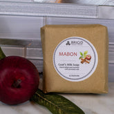 A bar of natural goat's milk soap with 'MABON' labeled on it, surrounded by apples.