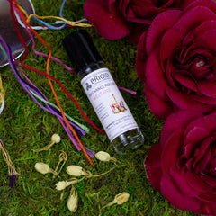 beltane perfume roller bottle oil roller for her for him for them rose jasmine clary sage and frankincense hand made natural celtic inspired made in kitsap county washington state image shows a moss background with a red flower and jasmine flowers with maypole and bottle of fragrance roller bottle essential oil blended fragrance
