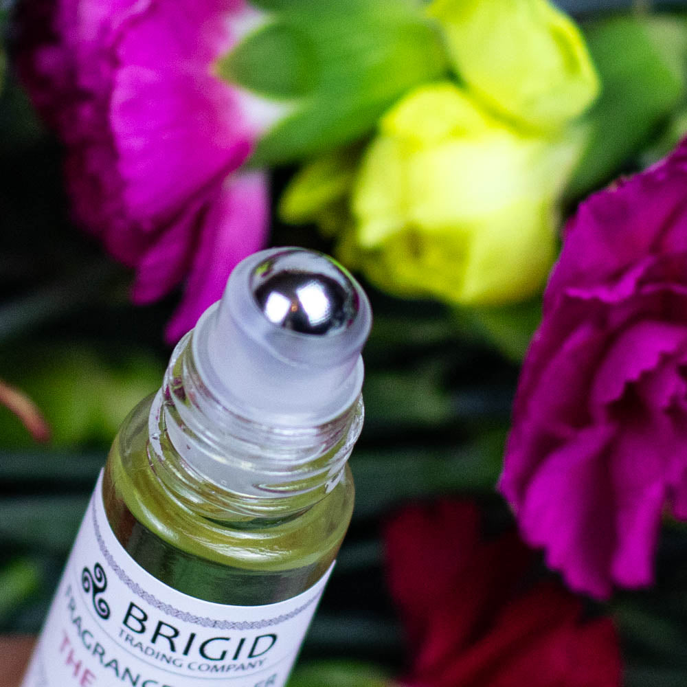 fragrance roller oil scent roller perfume bottle by brigid trading company llc jojoba oil, castor oil, essential oils only aromatherapy clean ingredients amber bottles with flowers in the background celtic holidays scents clean roller bottle close up metal ball