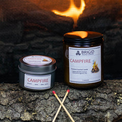 campfire mesquite smoke warm woods scented candle for camping fans mens gifts womens gifts for her for him outdoor fan presents hiking is in tents hand made in kitsap county independent american owned business usa grown sustainable soy wax not tested on animals original studio image by brigid trading company photography image shows two candles large and small with fire in background, matches and wooden log