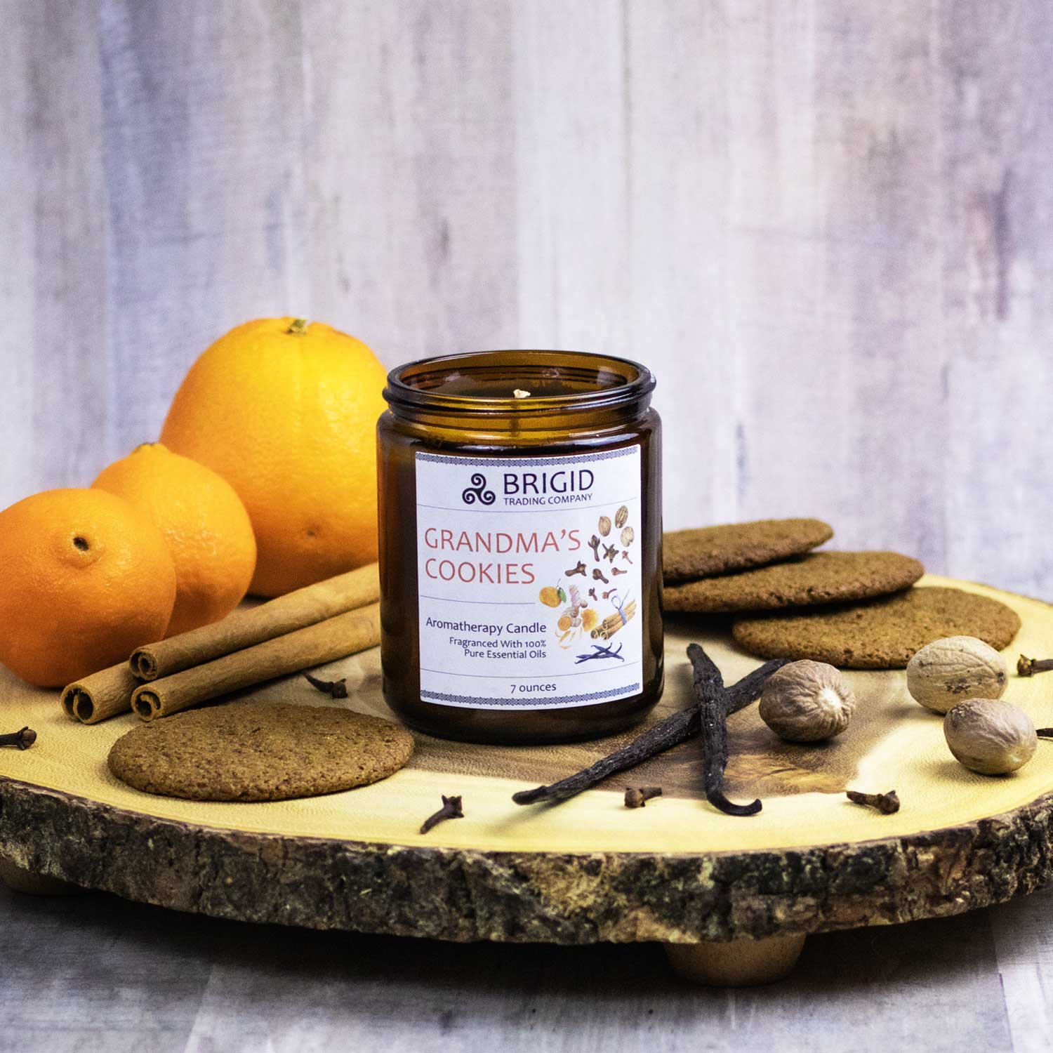 grandmas cookies aromatherapy candle by brigid trading company llc essential oil candles natural soy wax hand poured studio shot of candle in glass jar on a wooden cutting board with oranges cinnamon sticks cookies vanilla bean whole nutmeg and cloves