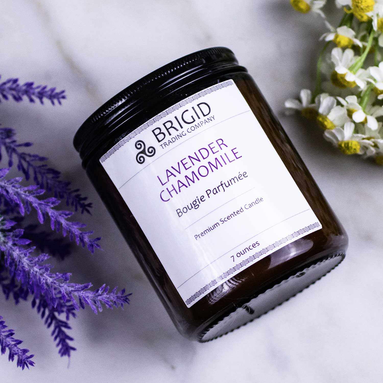 lavender chamomile bougie parfumee premium scented candle by brigid trading company soy wax hand poured hand made glass jar candle background is clouds with lavender and chamomile flowers and candle product photo in center with marble tile background