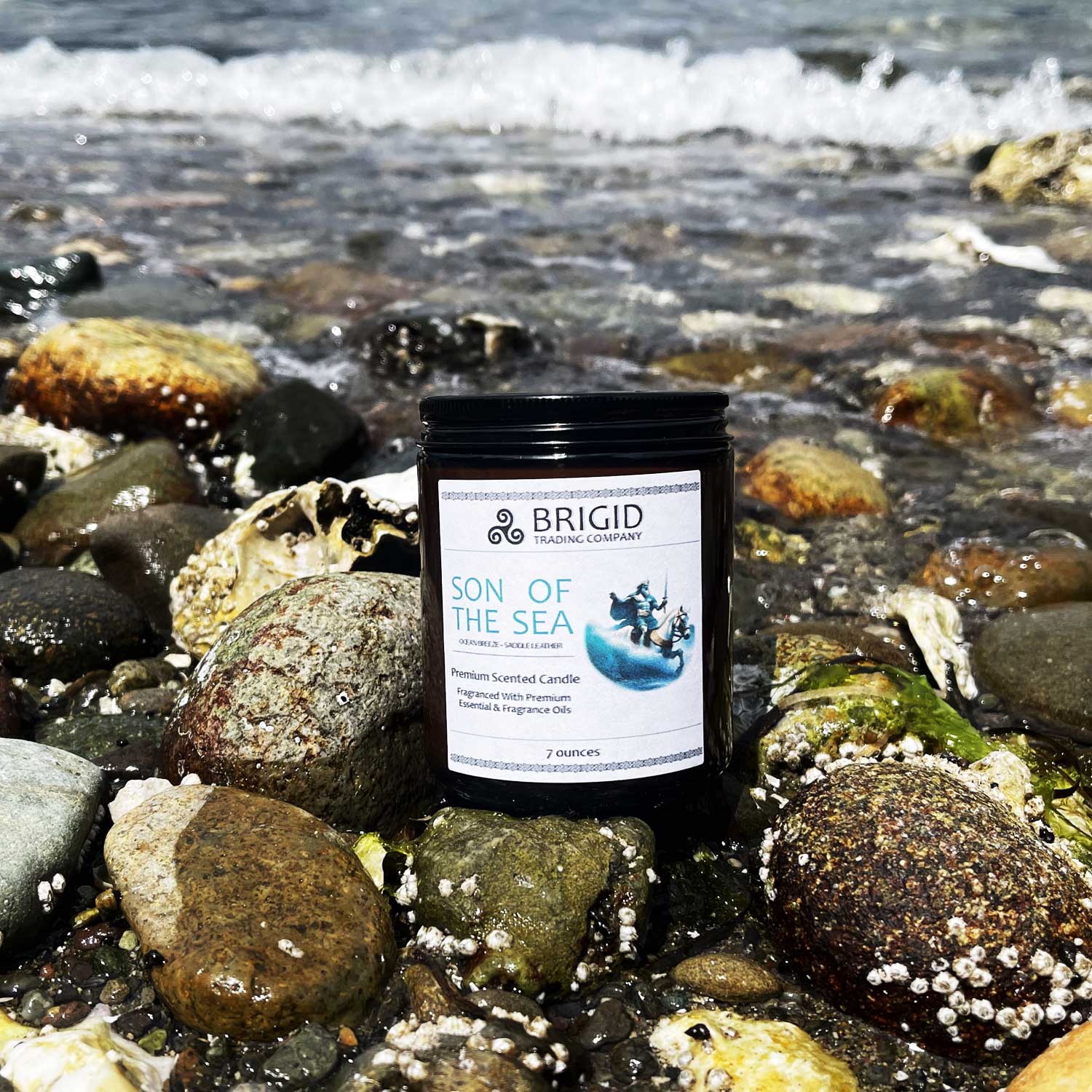 son of the sea candle by brigid trading company mannanen mac lir celtic mythology story candle ocean mist and saddle leather scent made in kitsap county washington state usa amber jar with art label on the beach rocks with wave in background scenic beach