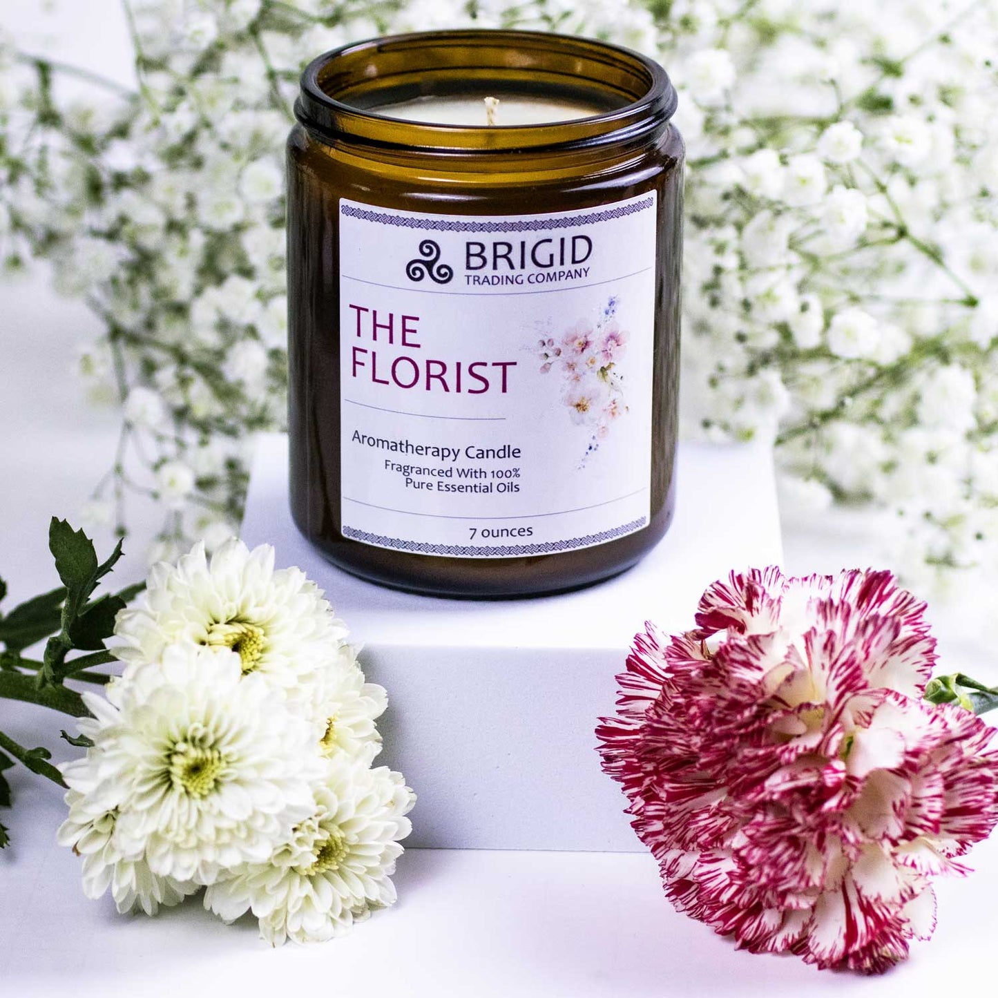 the florist premium aromatherapy grade essential oil candle candles by brigid trading company washington state united states ireland seven ounces kitsap therapy therapeutic benefits natural health white babys breath background with white flowers and pink flowers in the foreground candle in center