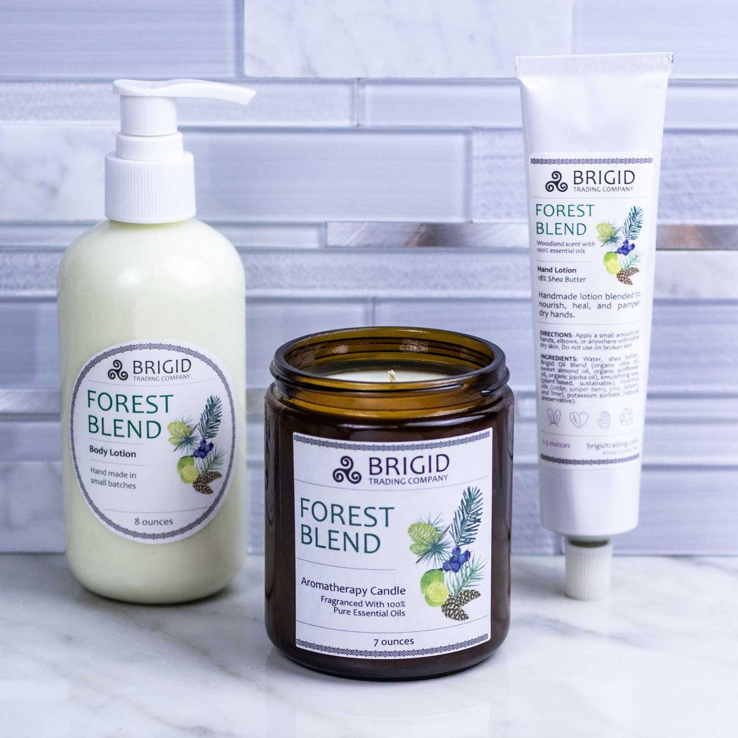 forest blend gift set by brigid trading company llc balsam juniper berry and pine scented body lotion aromatherapy candle and hand lotion depicted in studio shot of countertop with ceramic tile and glass backsplash