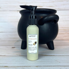 Bottle of Brigid Samhain body lotion with a pottery colored container on a wooden surface in front of a black cauldron