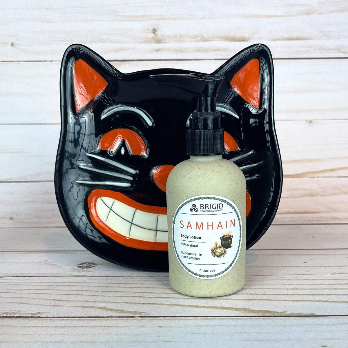 Bottle of Brigid Samhain body lotion in front of a black cat-shaped plate on a wooden surface