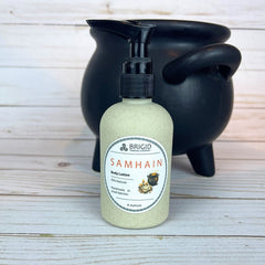 Body lotion bottle labeled 'Samhain' by Brigid with a black cauldron on a wooden surface.