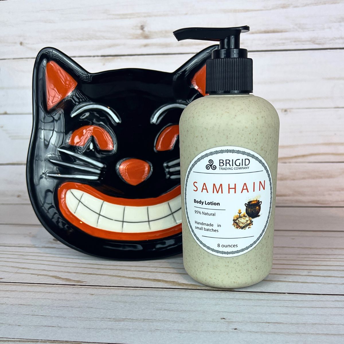 Body lotion bottle with 'Samhain' label next to a black cat-shaped plate on a wooden surface