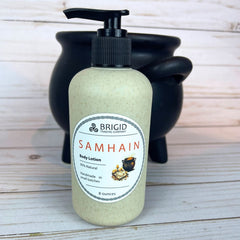 Body lotion bottle with pump labeled 'Samhain' by Brigid Trading Company on a wooden surface in front of a black cauldron