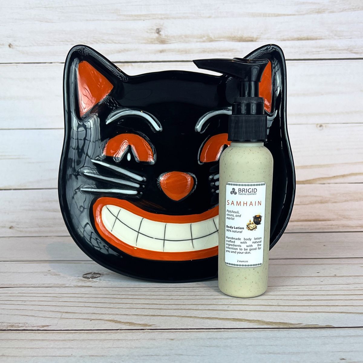 Black cat-shaped plate with a bottle of Brigid Samhain body lotion in front of it on a wooden surface