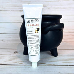 Tube of Brigid Samhain hand lotion in front of a black cauldron on a wooden surface