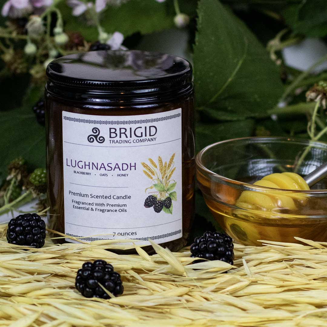 lughnasadh candle 7oz by brigid trading company llc blackberry oat honey scent premium soy wax candle photography original by brigid trading company blackberry leaves and plants in background with fresh blackberries sitting on dried oats with bowl of honey and honey spoon next to candle in amber glass jar with lughnasadh on the label 2024 kitsap county washington state united states