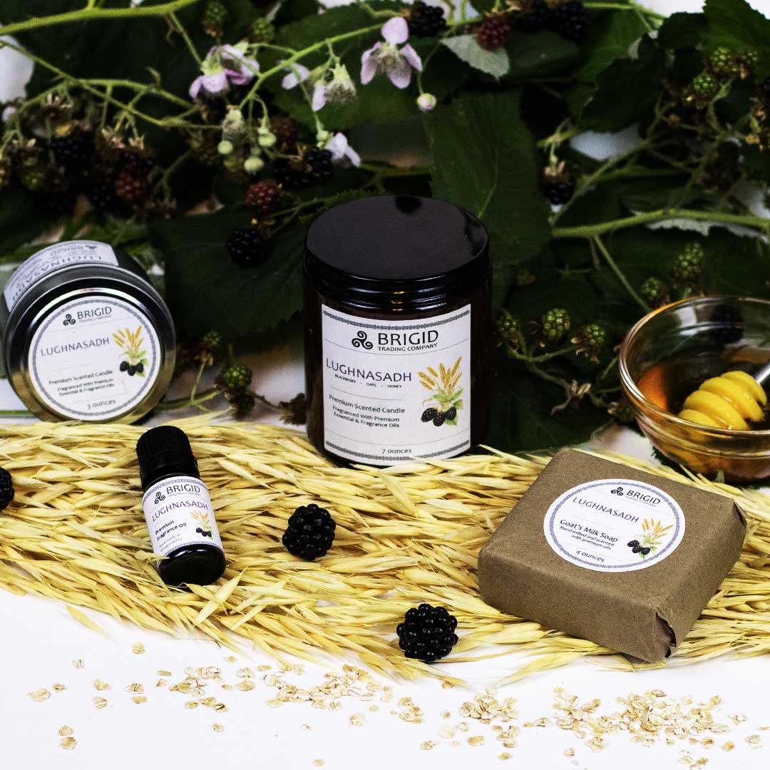 lughnasadh fragrance a bar of soap two sizes of soy wax candles and a diffuser oil bottle from brigid trading company all scented with blackberry fresh oats and honey arranged on a natural backdrop of fresh blackberries oatstraws and a wooden honey dipper